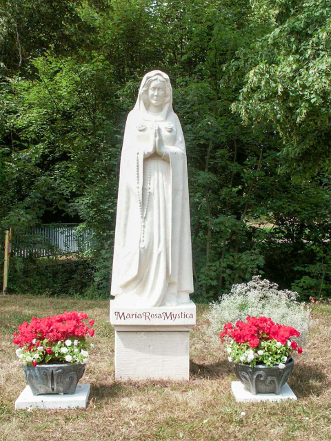 Eine Madonnenstatue aus weißem Stein aufgestellt im Freien.