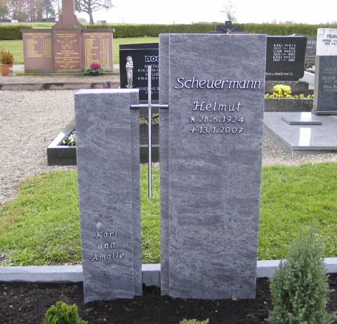 Zwei hohe, schmale Grabsteine, die mit einem schlichten Metallkreuz verbunden sind